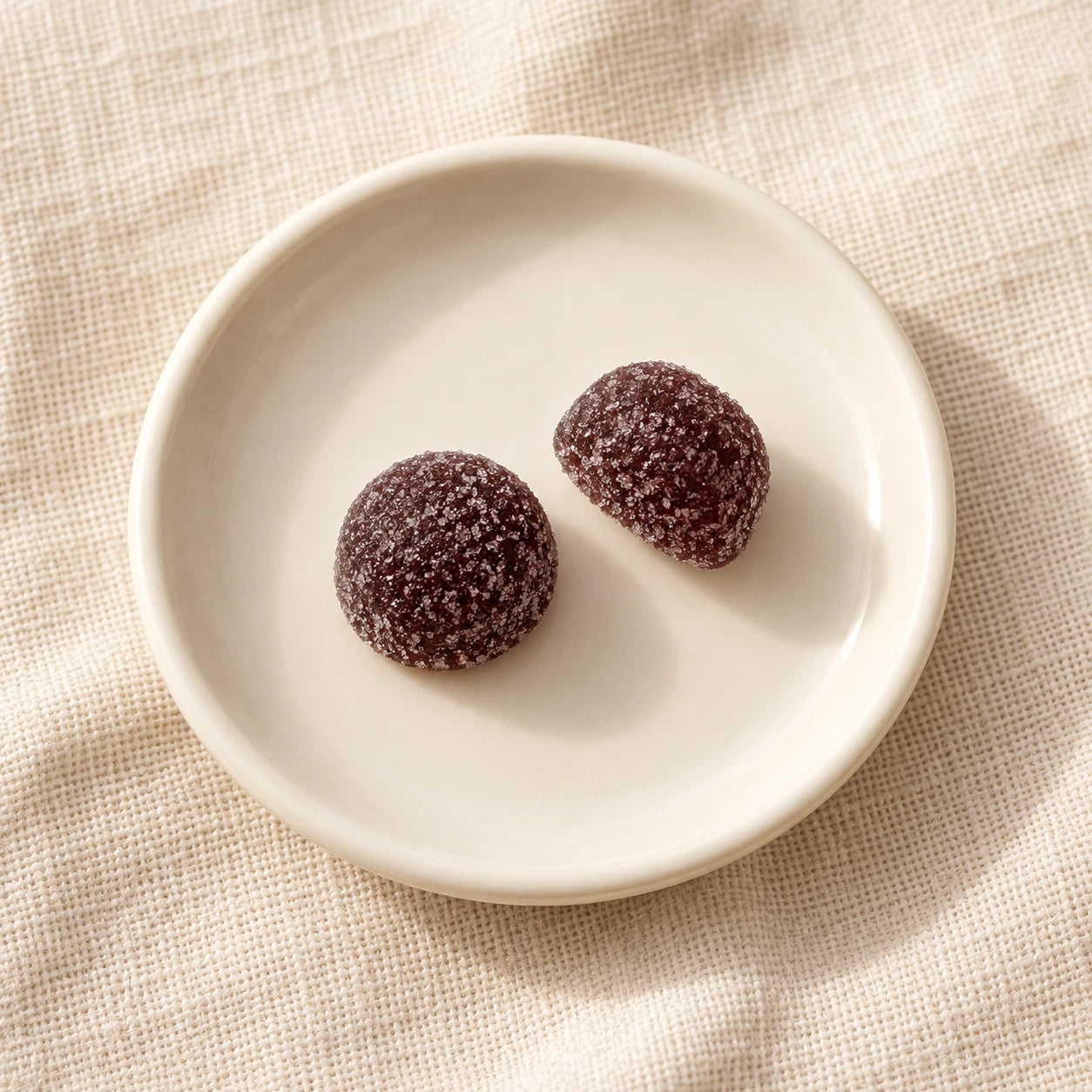 Exactly two grape gummies on an ivory saucer